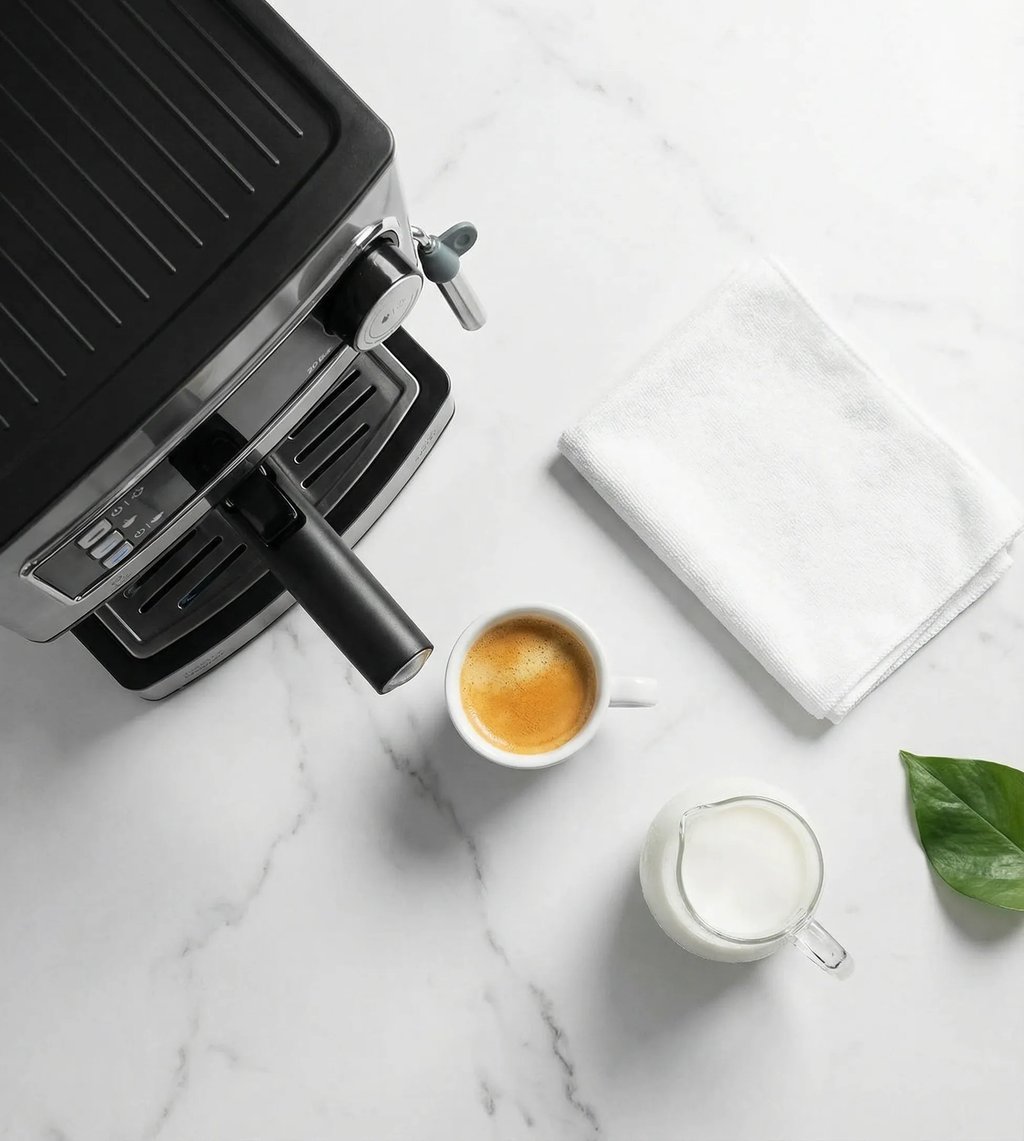 Espresso servido junto a una jarra de leche y un paño, al lado de la cafetera