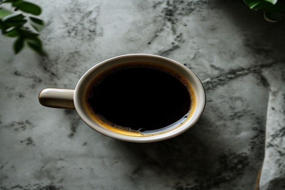 Taza de café negro frío visto desde arriba sobre una encimera de mármol