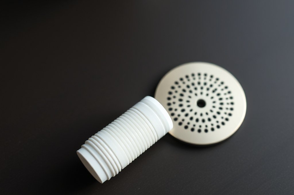 Cartucho filtrante de agua blanco junto a la ducha del grupo perforada, las dos piezas que se confunden