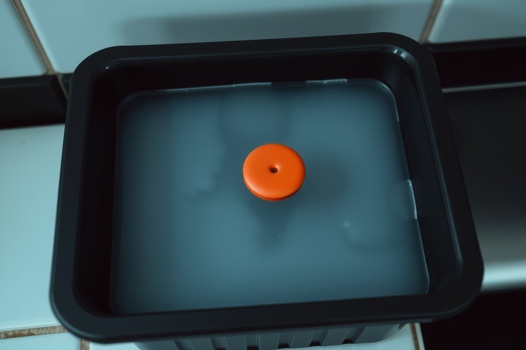 Bandeja de goteo negra rebosante de agua gris turbia con el disco rojo del flotador asomando