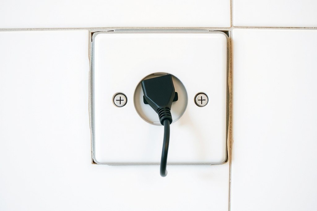 Enchufe de pared sobre azulejo blanco con la clavija de un electrodomestico conectada: lo primero que hay que descartar cuando la cafetera no enciende